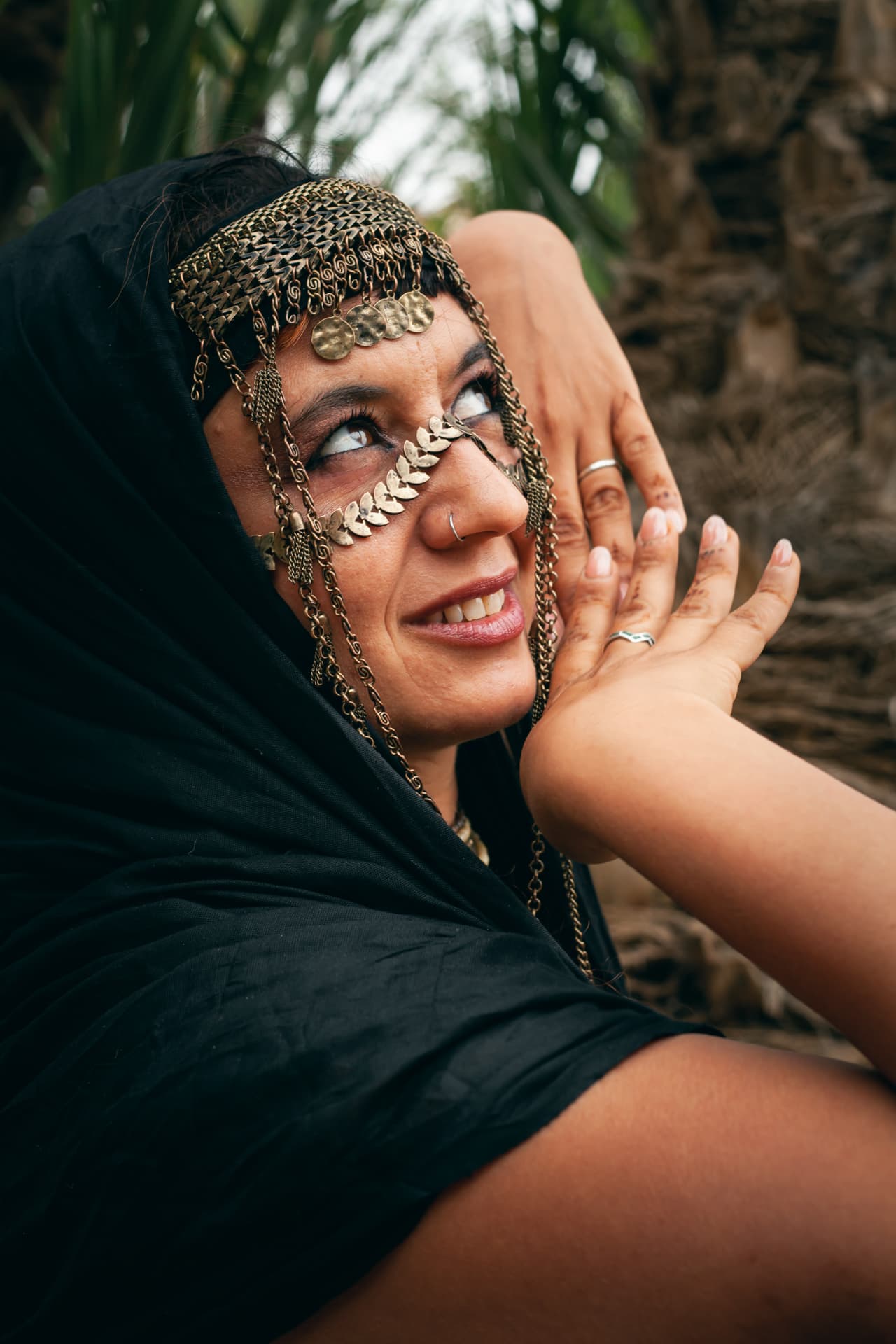 Laila glimlachend met hoofdsieraad van muntjes, ingesloten door zwarte doek